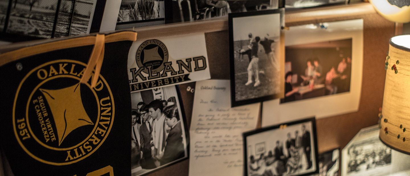 multiple black and white photos and Oakland University memorabilia hanging on a cork board
