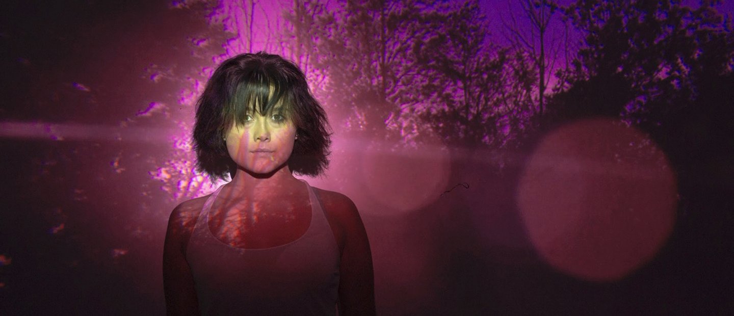 woman standing in front of an image of trees with purple and red lighting
