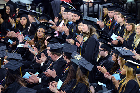 Students in caps and gowns clapping at a commencement ceremony