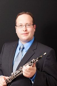 man in a suit, holding an oboe, smiling at the camera