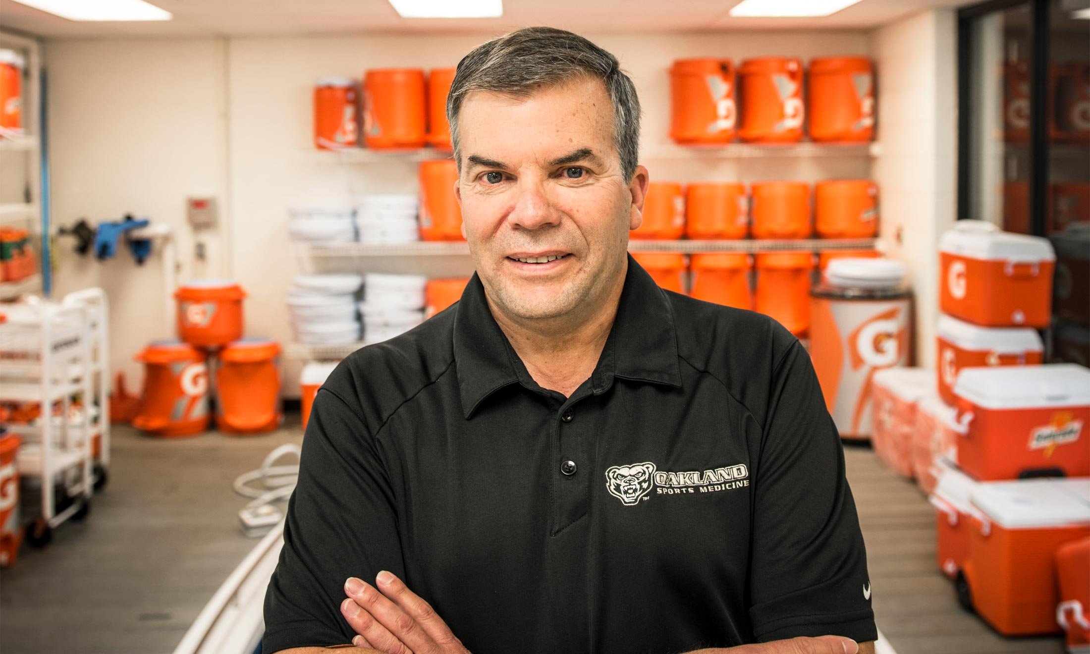 Oakland University athletics trainer Tom Ford stands in front of orange water coolers in a water training room