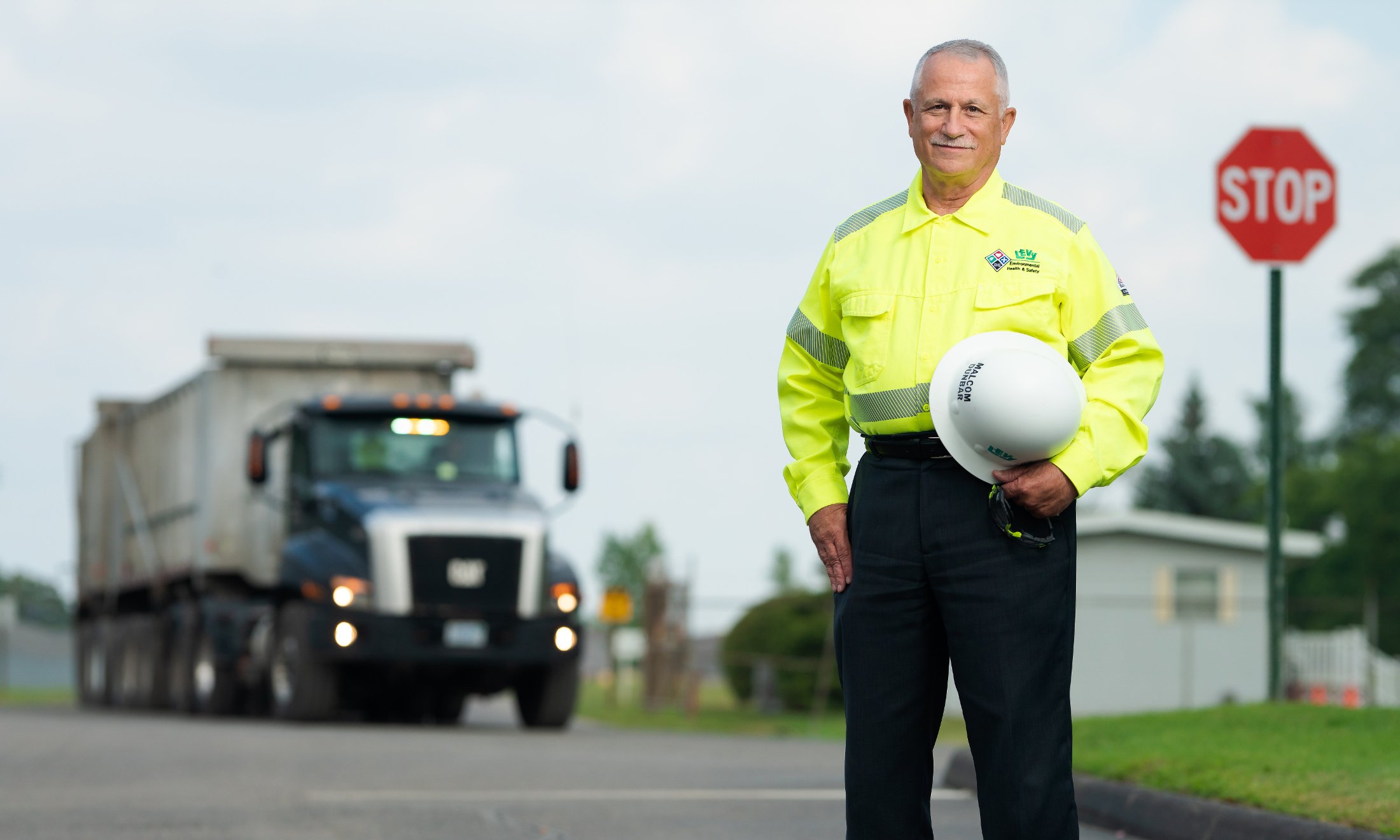 Malcom Dunbar stands by a dump truck, wearing a high vis helmet and holding a hardhat