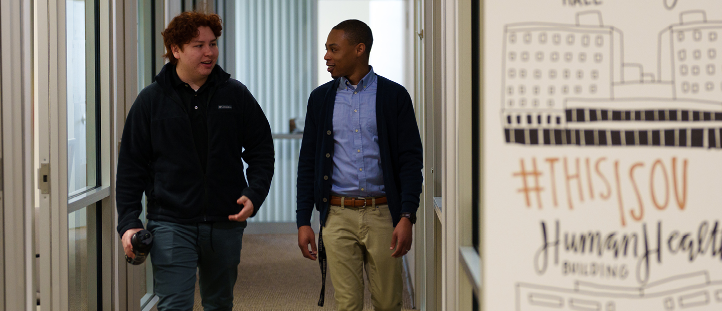 Two young men walk together down a hallway in a building on O U's campus.