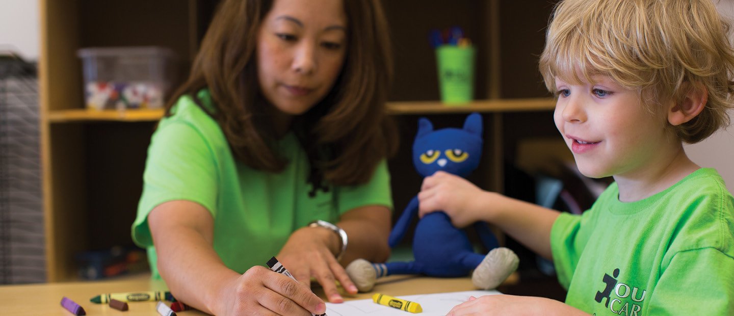 Woman and young child in bright green shirts, coloring with crayons.