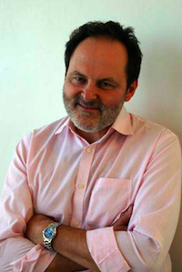 man in a pink shirt with his arms crossed, smiling at the camera