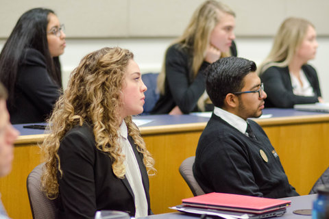 students in black professional attire, seated in rows in a classroom, all looking forward