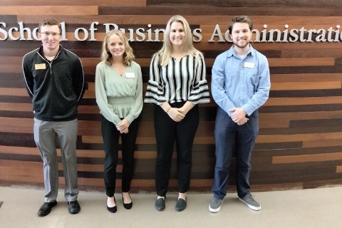 Business Scholars Nick Norman, Hannah Tucker, Alex Grenn and John Atkinson standing in front of a wall with "School of Business Administration" on it.