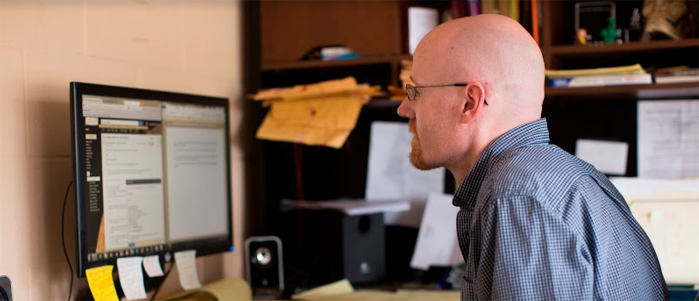 A man sitting at a desk, looking at a computer screen.