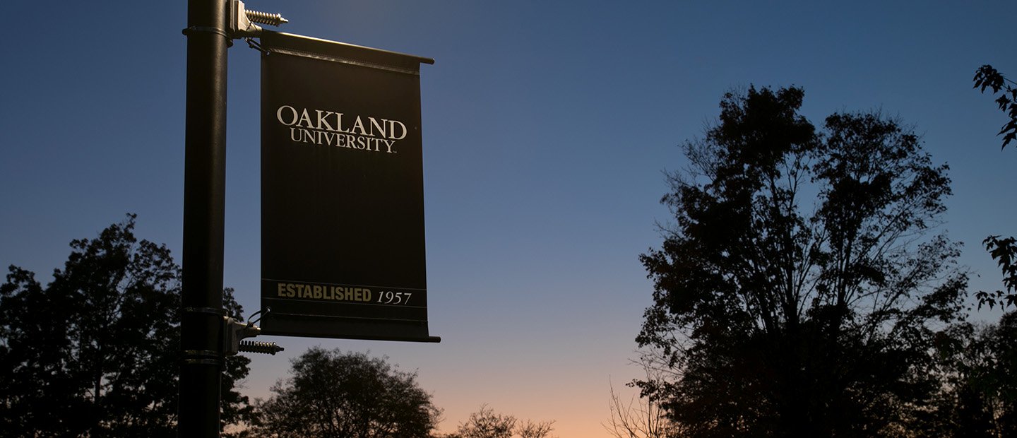 An Oakland University banner hanging on a pole outside at twilight.