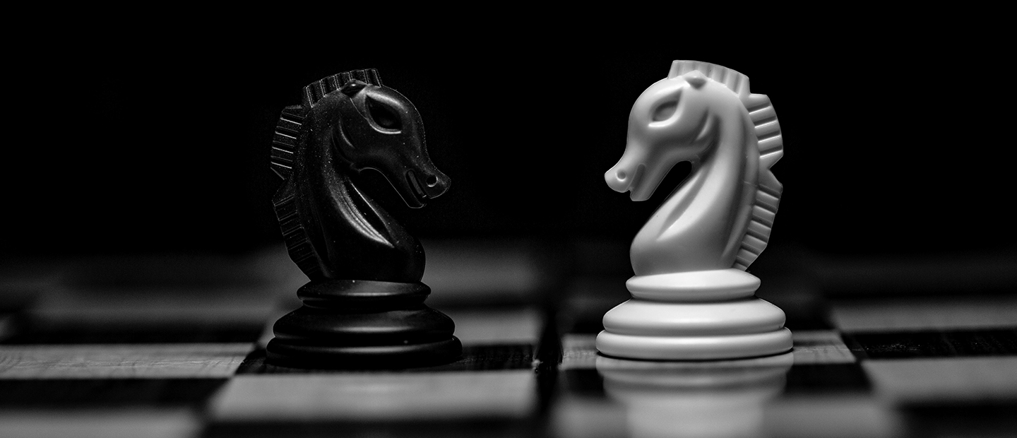 Two knight pieces facing each other on a chessboard, one black and one white.