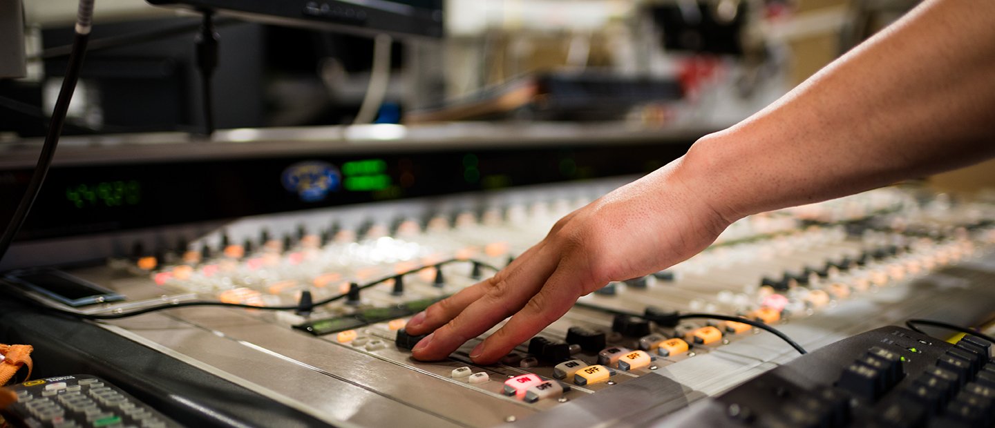 A person's hand working on a sound mixing board.