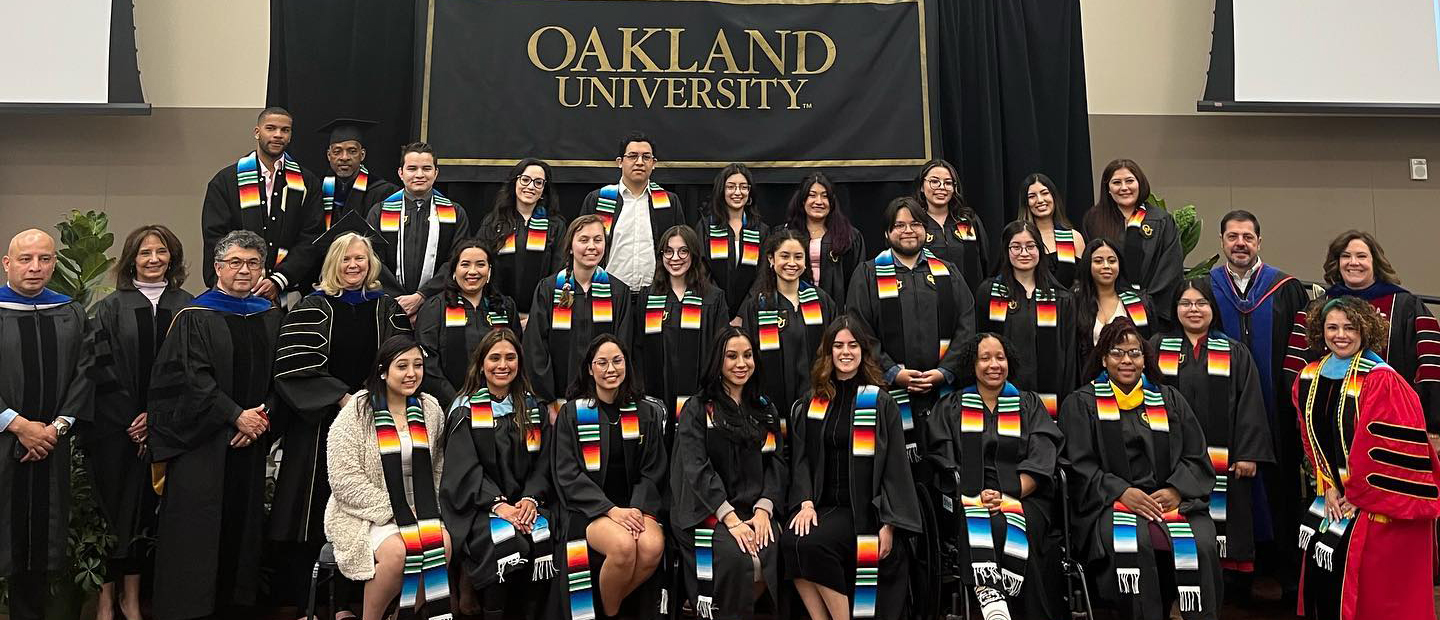 Oakland University graduates in gowns and sashes.