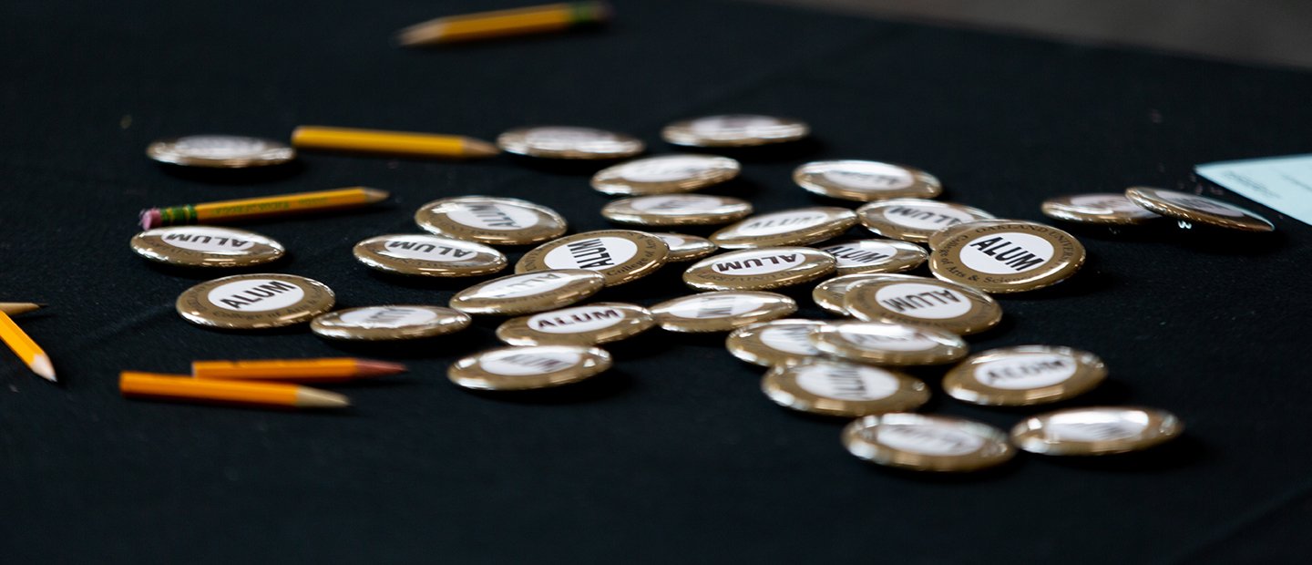 A bunch of round buttons that say Alum on them and a few pencils on a table.