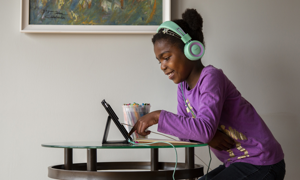 Image of a young child sitting in front of a computer with headphones on and smiling
