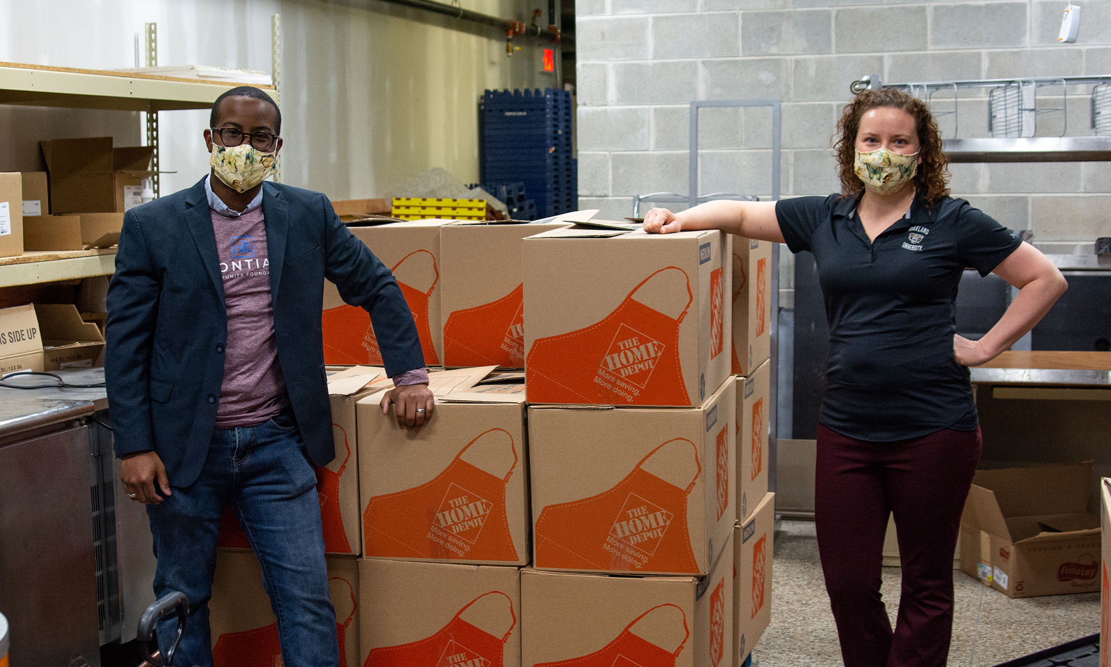 Two Oakland University employees standing next to boxes with masks on
