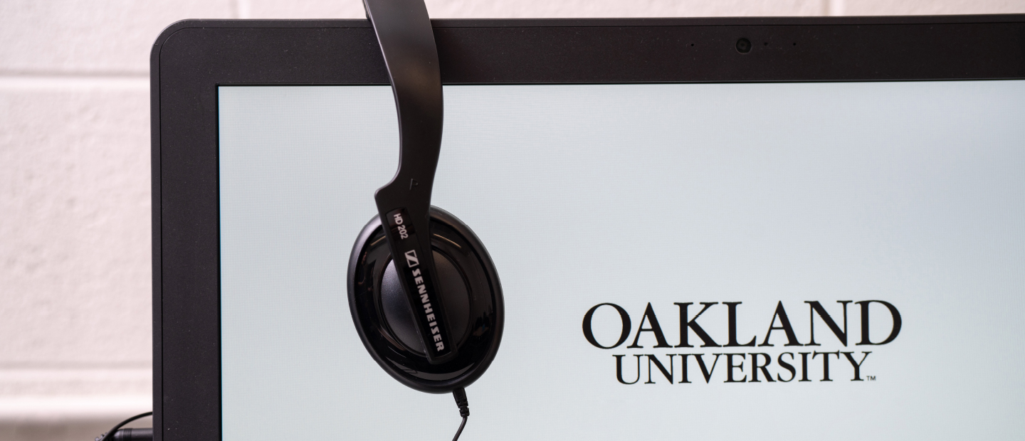 computer screen with Oakland University displayed and headphones hanging over the top