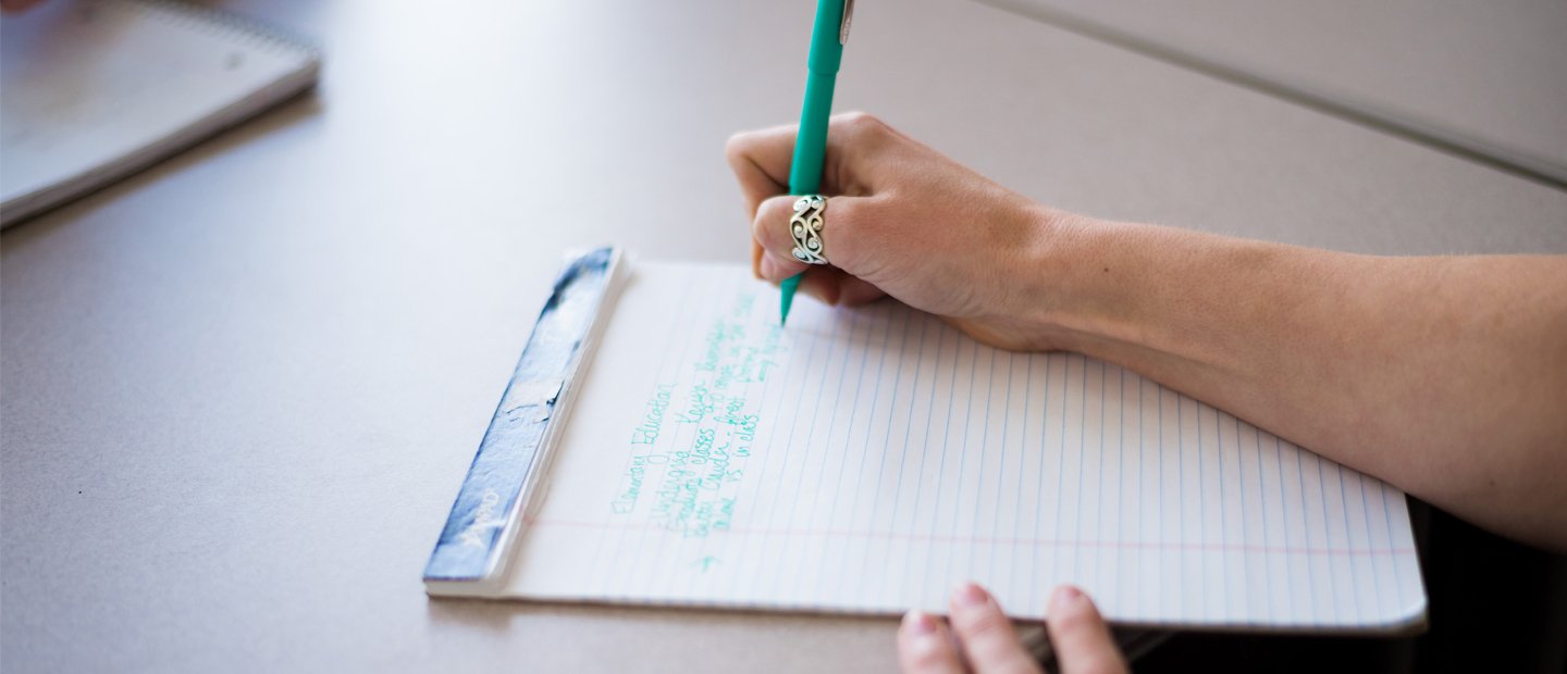 A person writing on a notepad with a green pen.