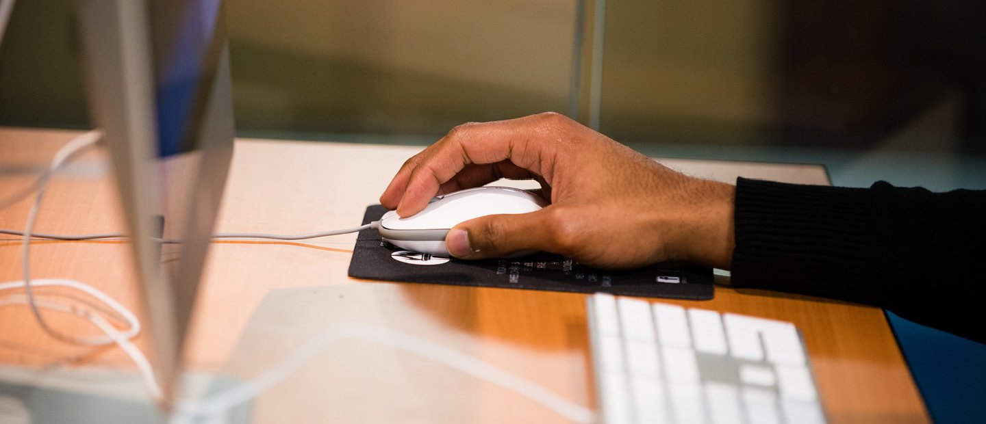 hand on a white computer mouse at a desk