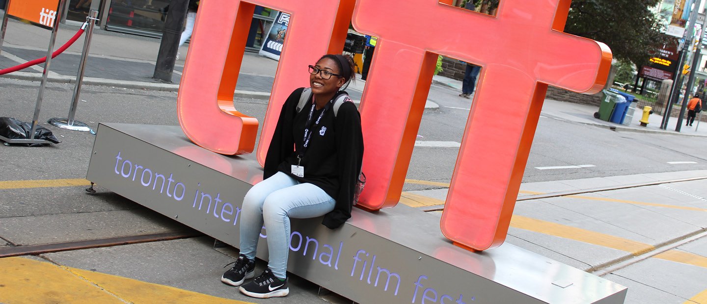 A student seated on a sculpture outside that says "tiff".