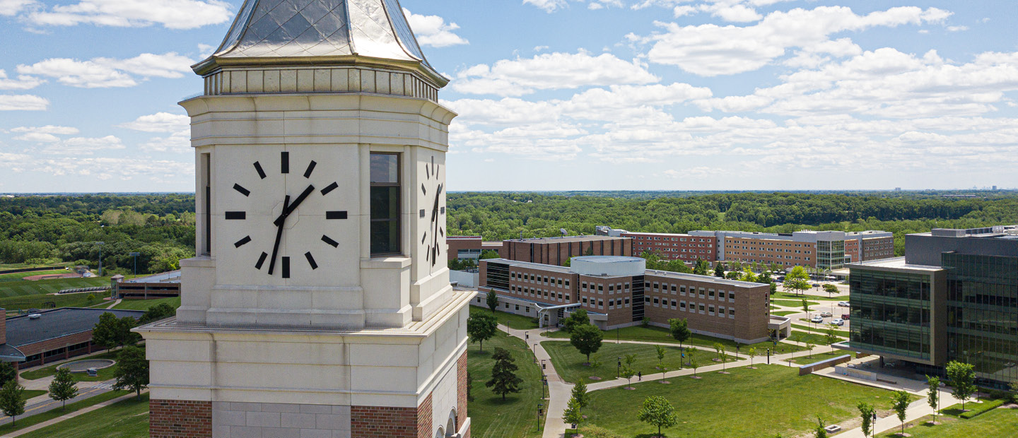 A photo of the clock face of Elliott Tower with Oakland University's campus in the background.