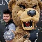 Ernesto Duran-Gutierrez, holding a First Generation Oakland University button, posing with the Grizz bear mascot..