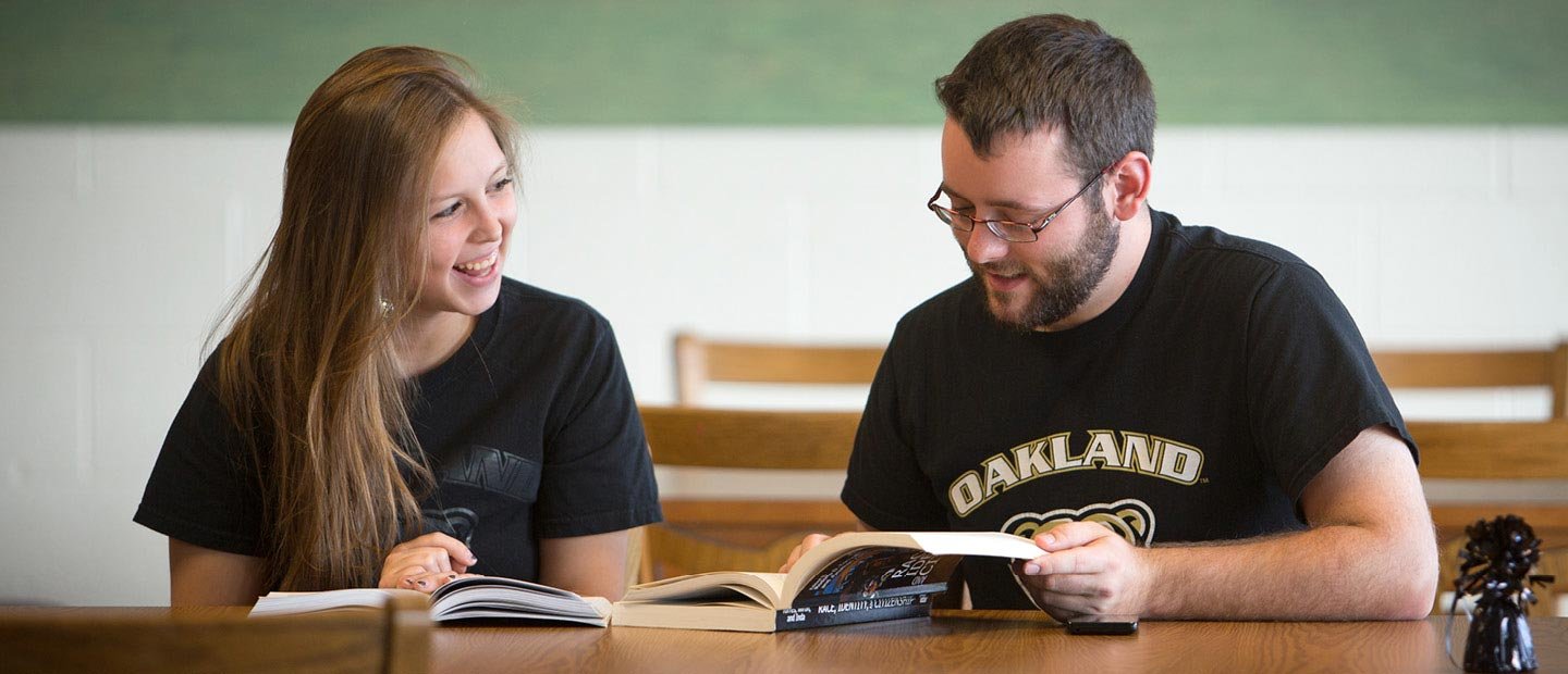 Students in black O U t-shirts reading textbooks at a table