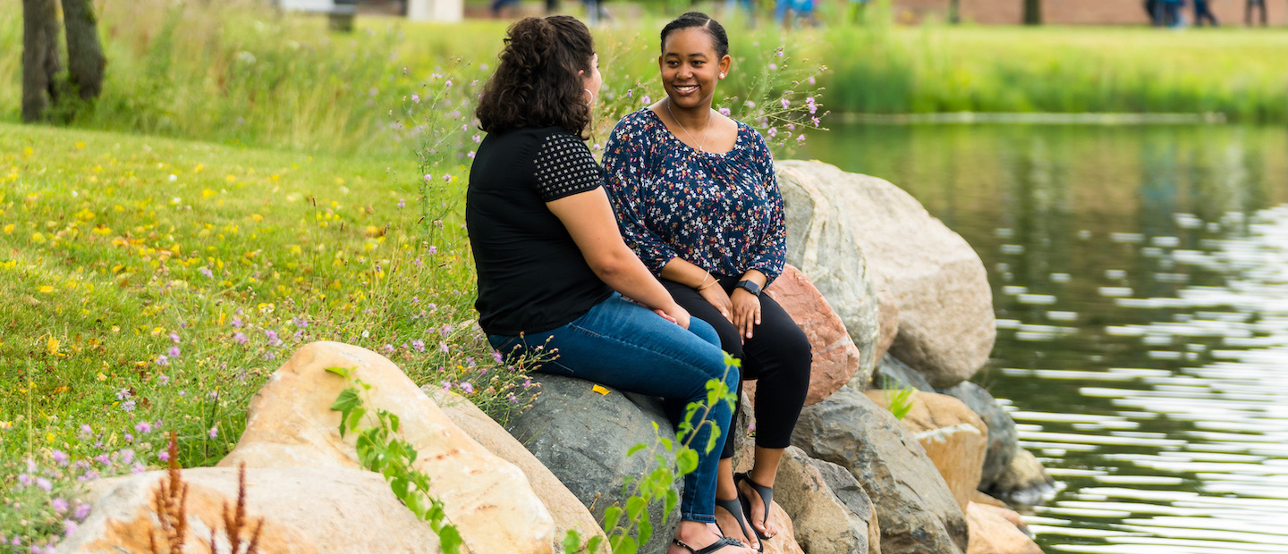 Two women seated on rocks at the edge of a pond at Oakland University.