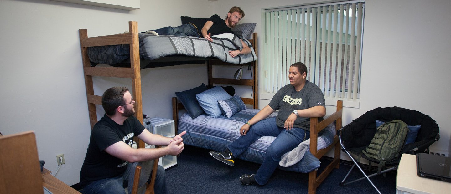 three men seated on furniture in a dorm room