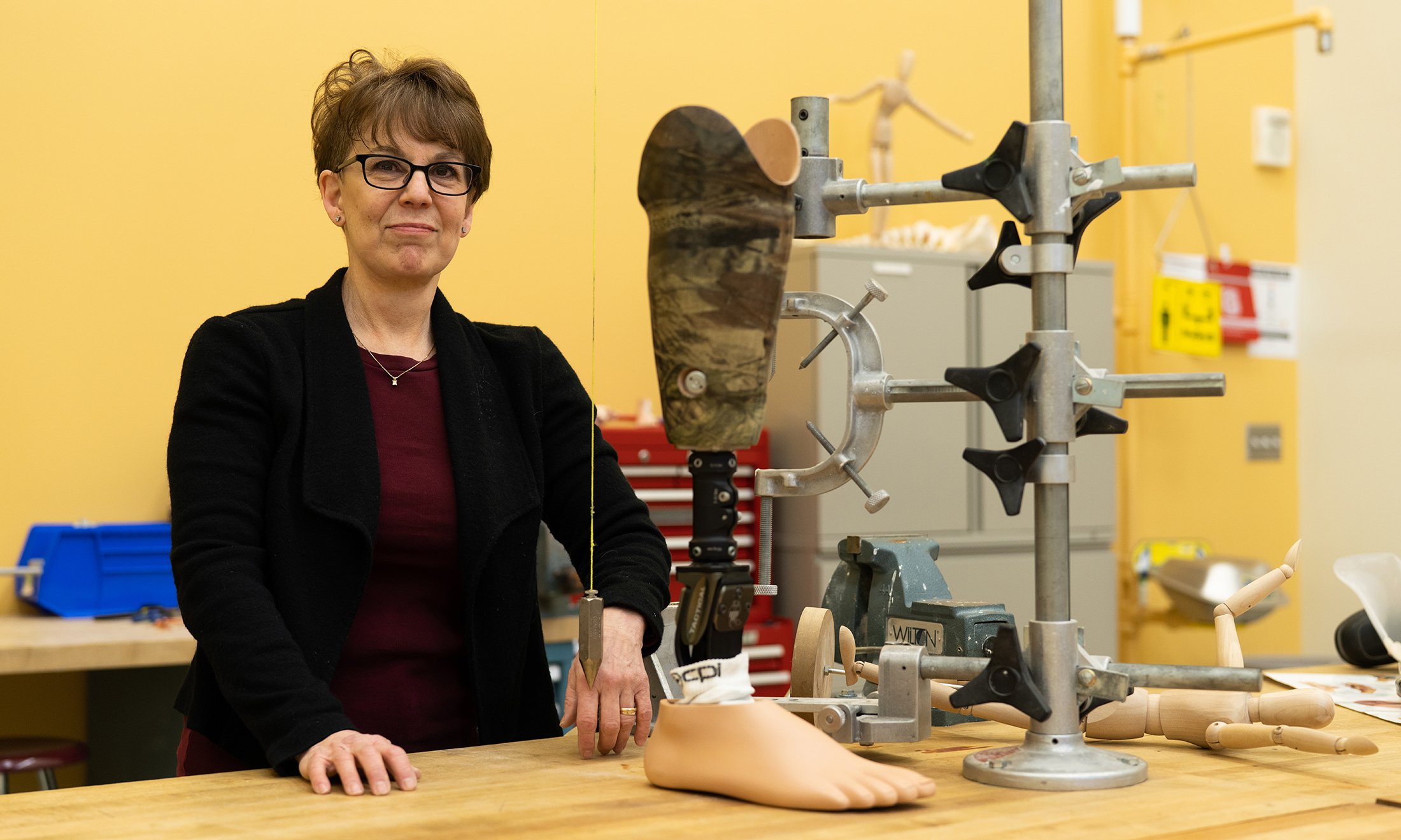 Woman standing next to a prosthetic leg in a lab