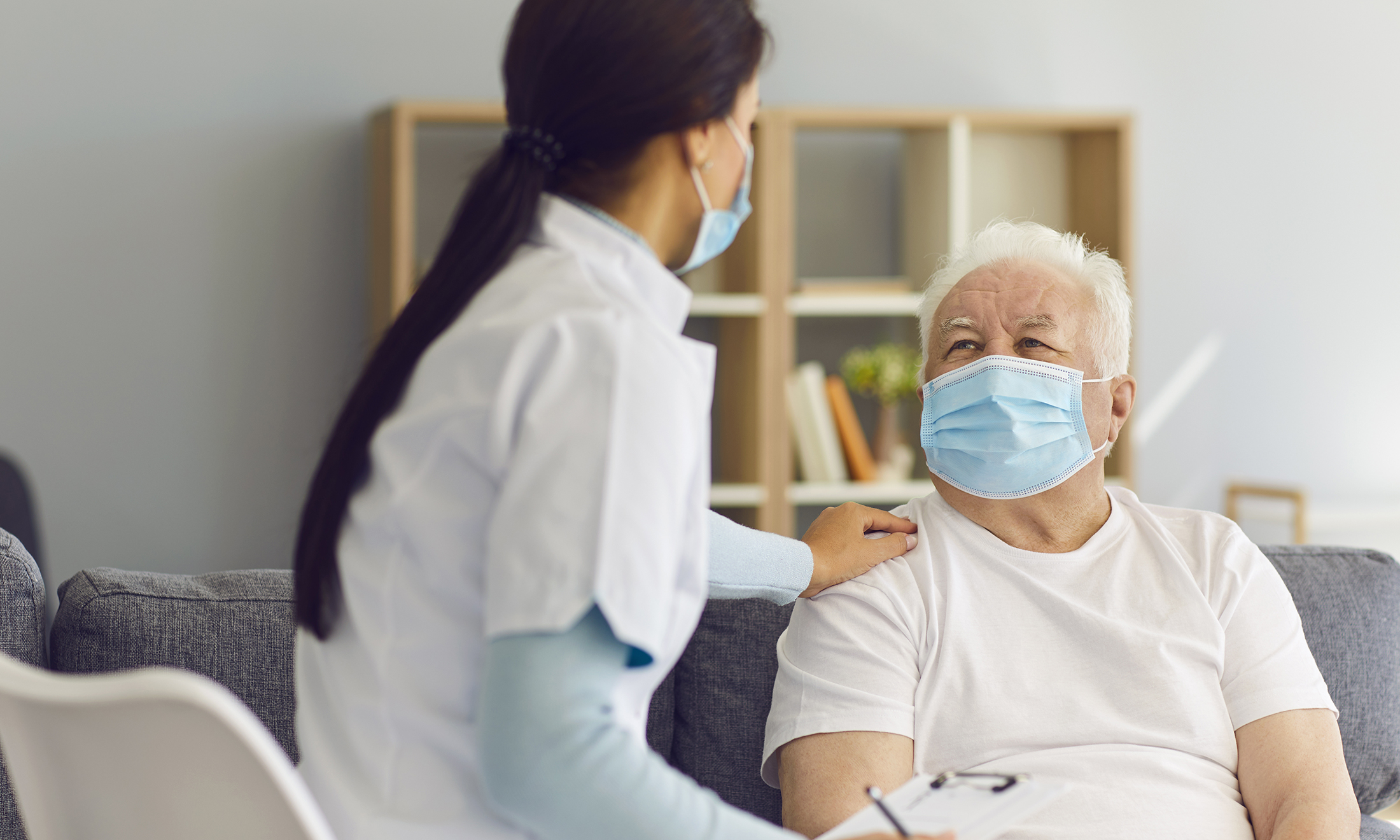 An image of a senior citizen wearing a mask and talking to a doctor