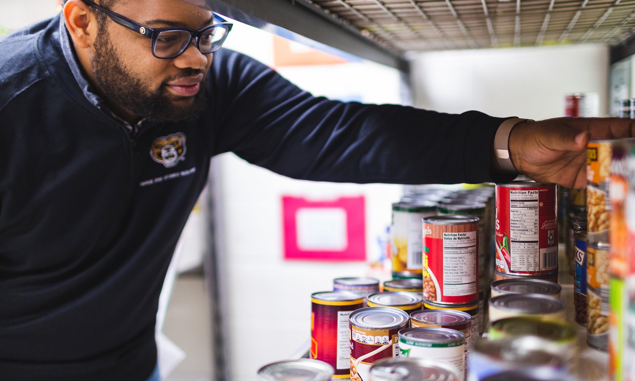 A photo of a man stocking shelves with canned goods.