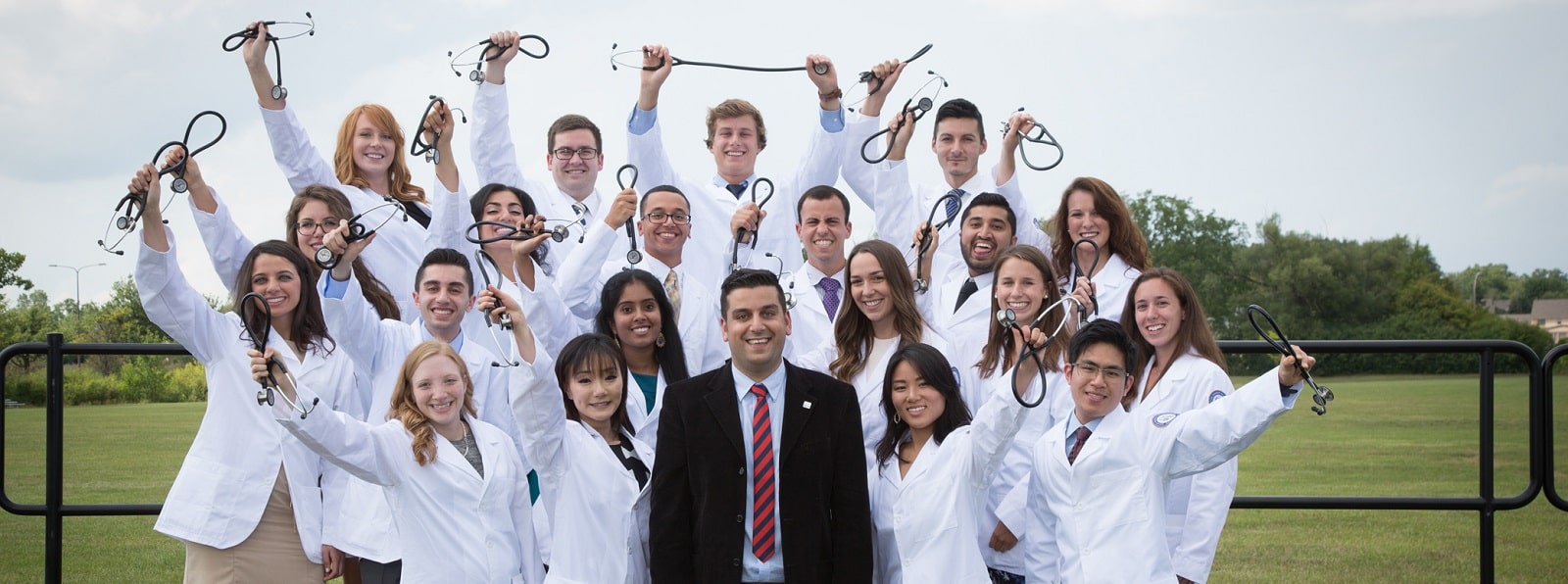 A PRISM group stands together wearing their white coats, smiling, and holding their stethoscopes above their heads.