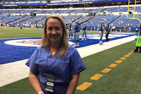 woman in blue scrubs standing on the sidelines at a football game
