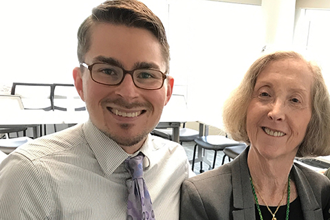 young man in a shirt and tie posing for a photo with an older female professor in a classroom