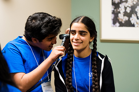 student using a medical instrument to examine another student's ear at the Diversity & Inclusion program