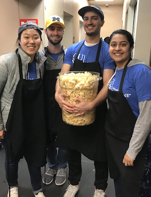 four students in blue O U W B shirts, holding a bucket of peeled and cut potatoes