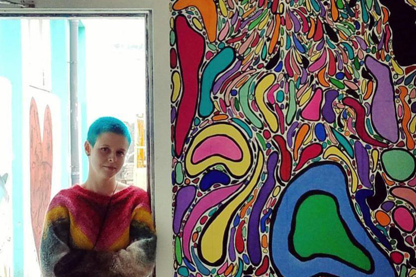 Chelsea Criger standing in an open doorway next to a wall covered in her art work in Iceland