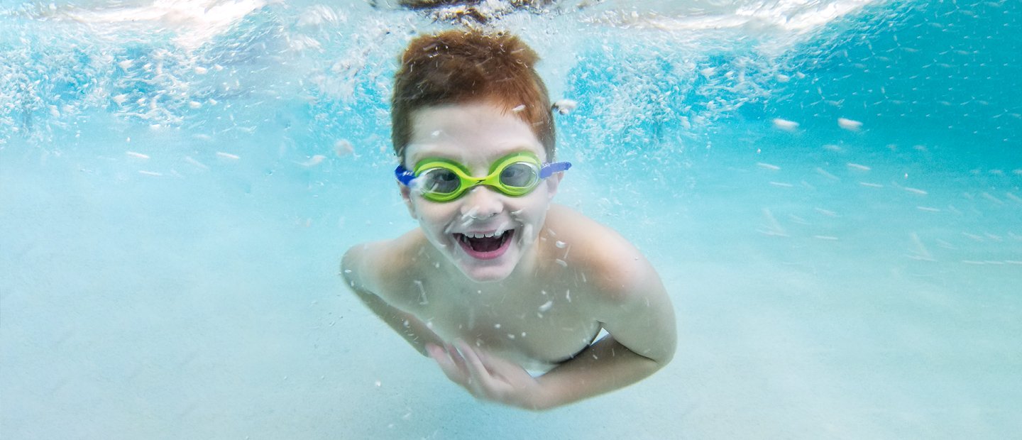 A child wearing goggles, swimming in a pool.