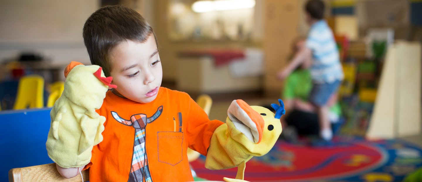 A young boy playing with two sock puppets in a classroom.