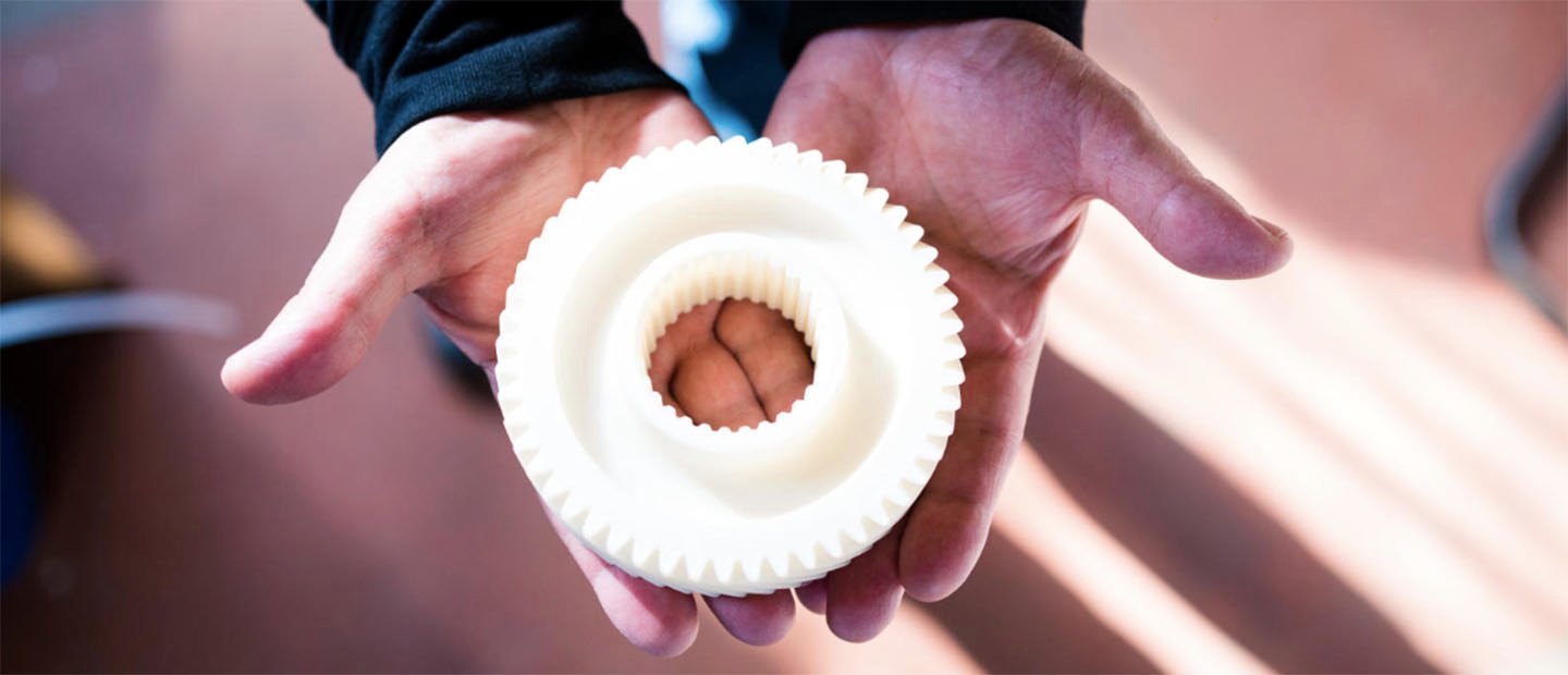 Two hands holding a round white donut shaped object with gear-like teeth around the edges.