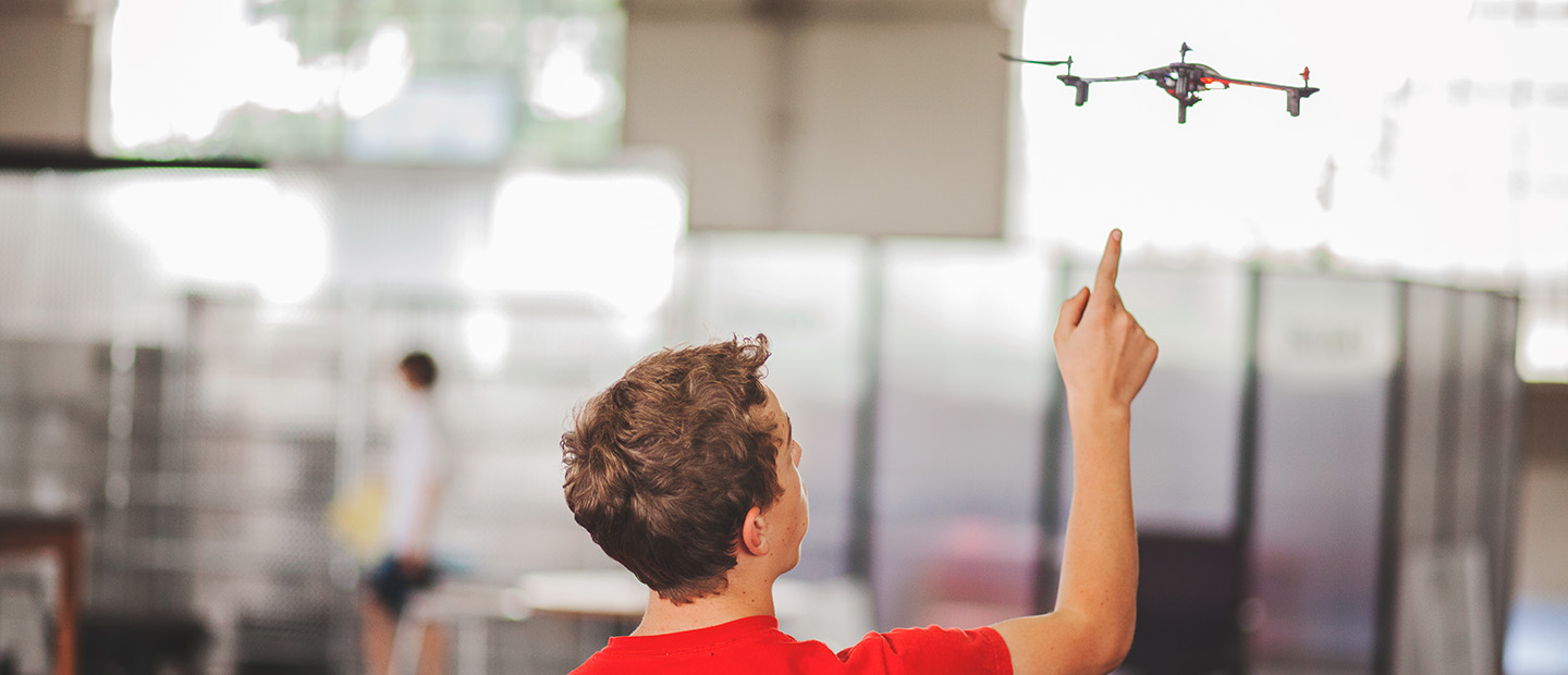 A young man pointing at a drone flying in front of him.