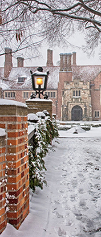 A winter scene of the walkway leading up to Meadow Brook Hall, both covered in a light snow.