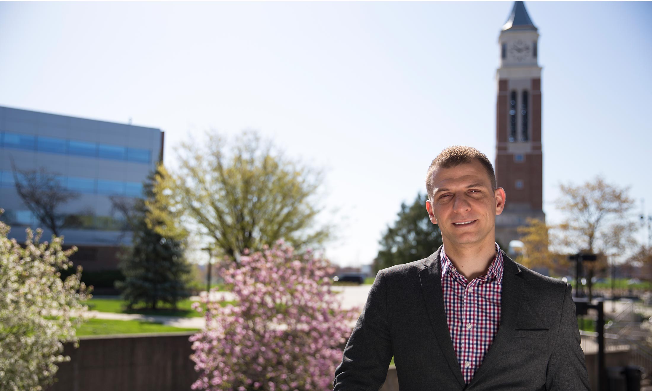 Oakland University graduate Sean Kosofsky poses for a photo during an afternoon on campus with Elliott Tower in the background