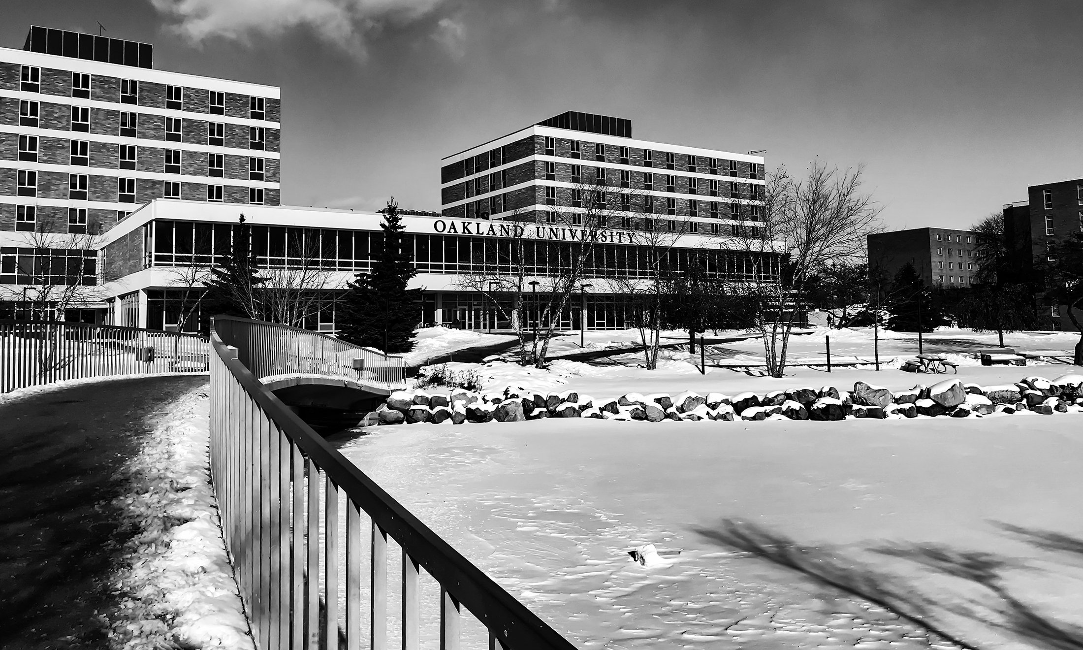 Black and white photo of Vandenberg Hall and bridge over bear lake in winter time. The lake is frozen and there is snow on the ground.