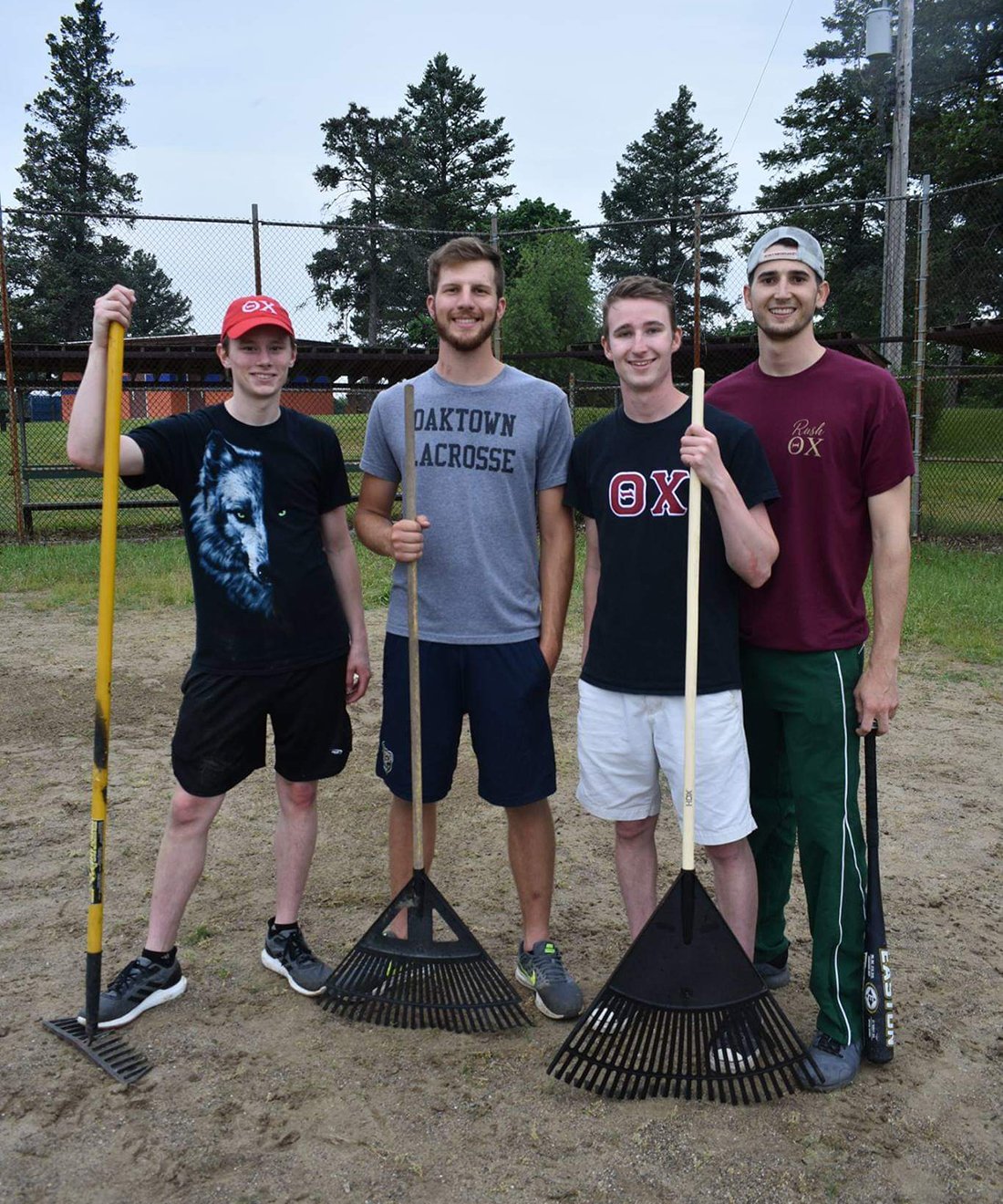 4 members of Theta Chi Fraternity with rakes in a park