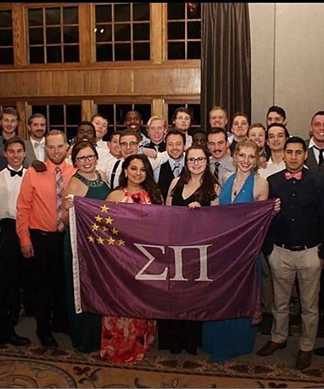 Members of OU fraternities and sororities in formal wear holding up a Sigma Pi flag at Meadow Brook Hall