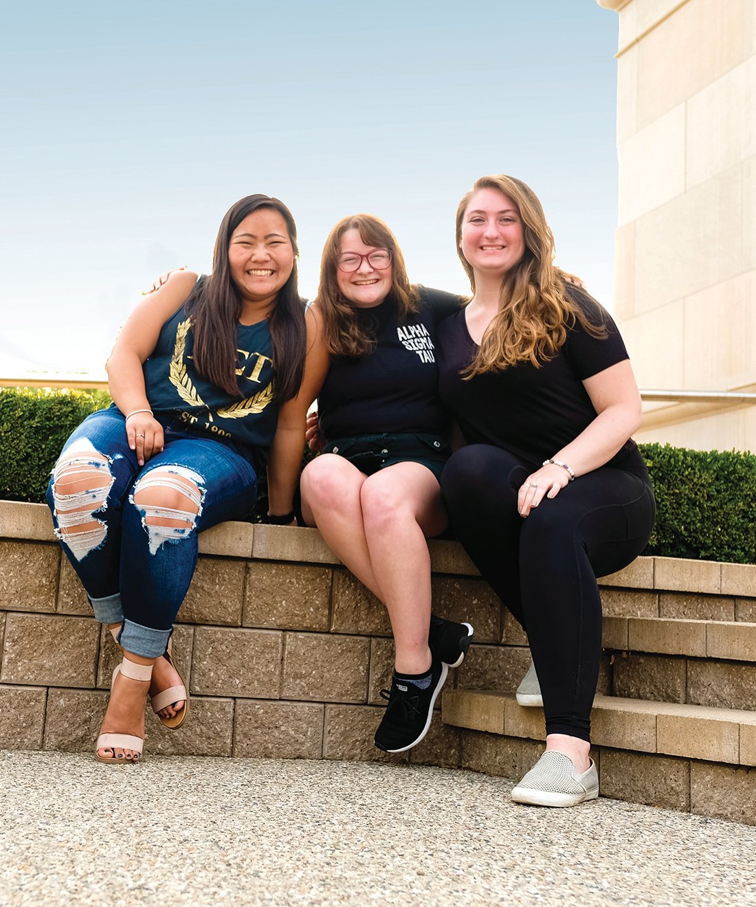 Three members of Alpha Sigma Tau sorority smiling and sitting on campus