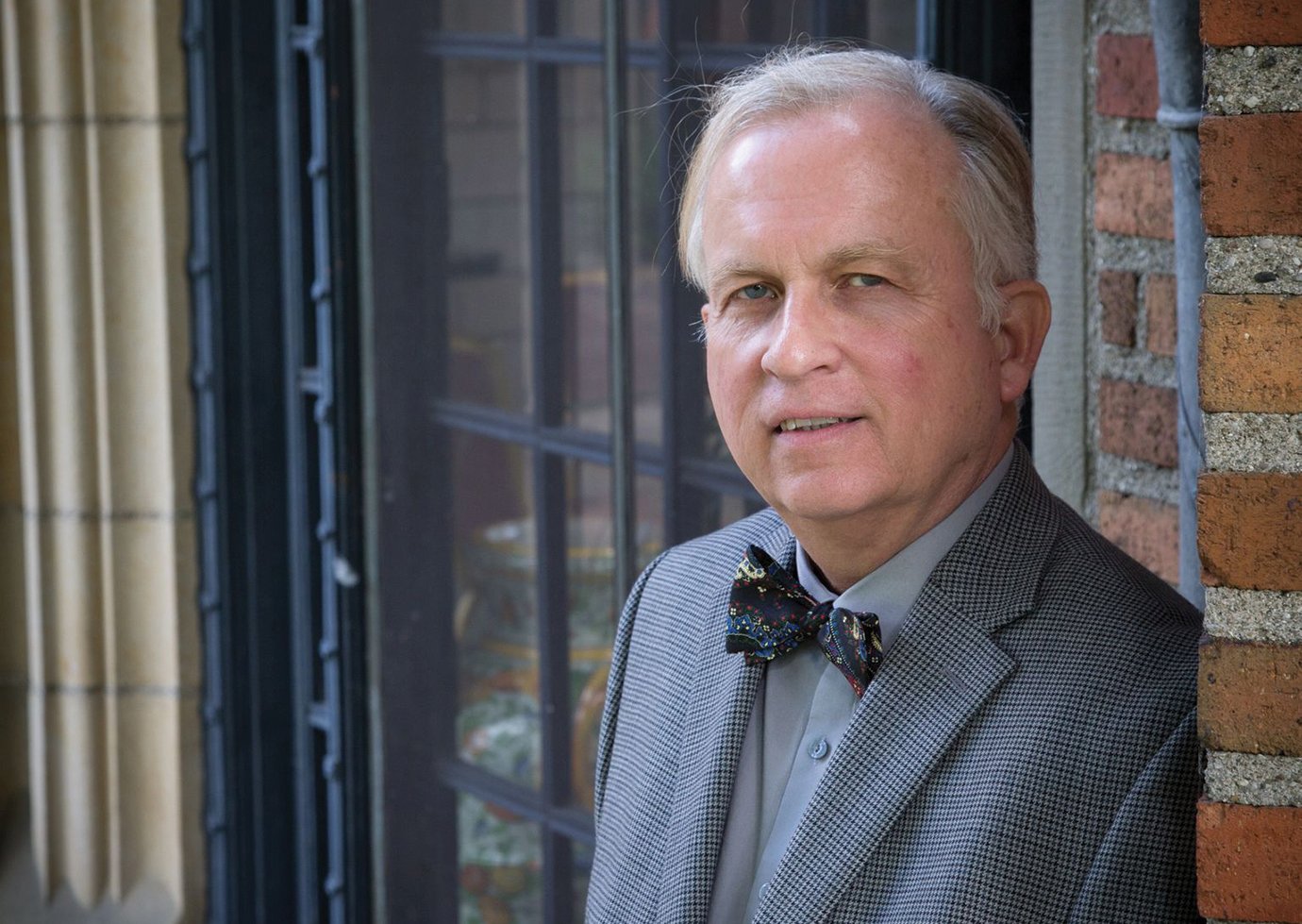 Mark Bowers dressed up with a bow tie leans up against a brick wall at Meadow Brook Hall