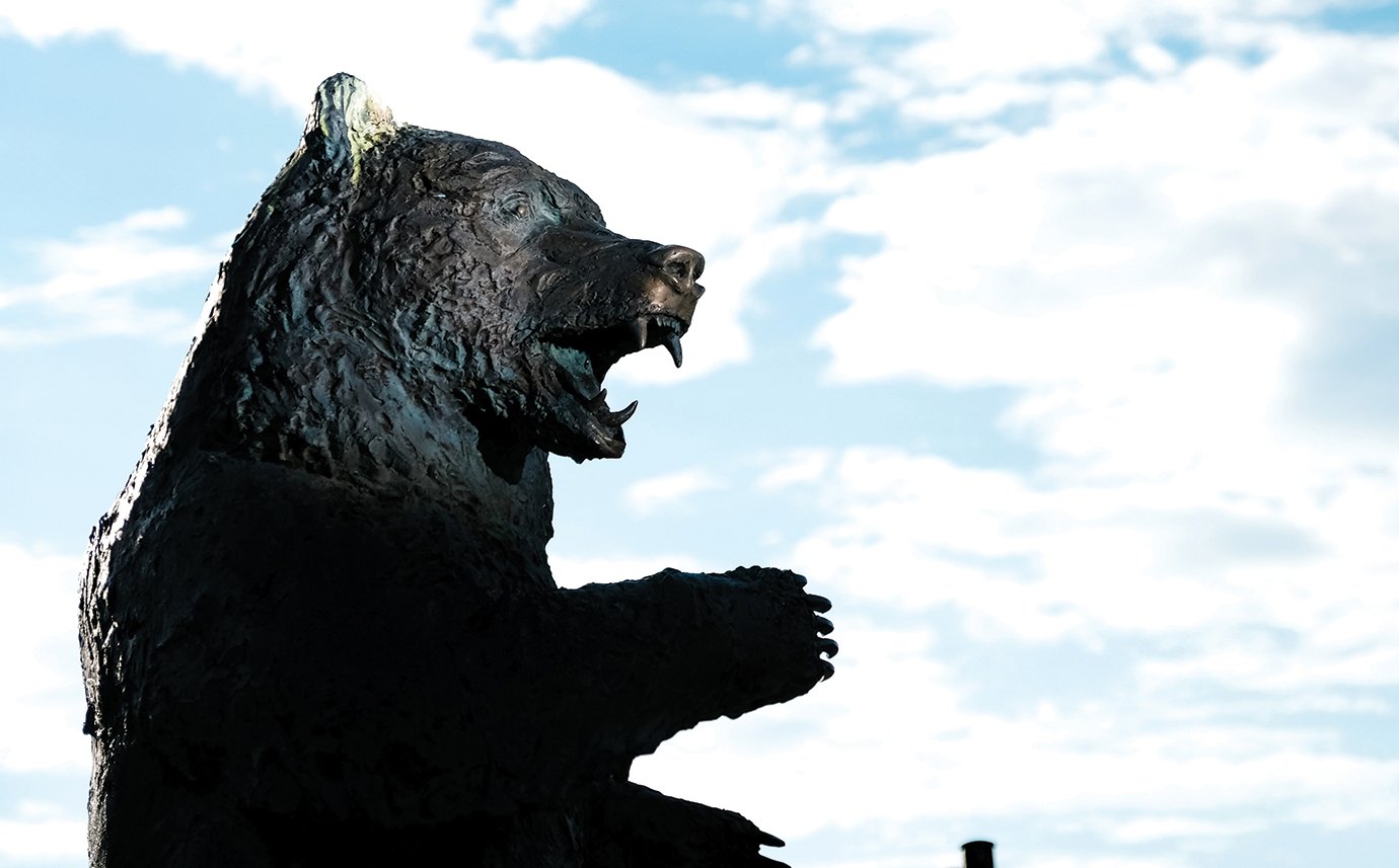 A grizzlie bear statue shows a side profile in front of a blue sky with white clouds