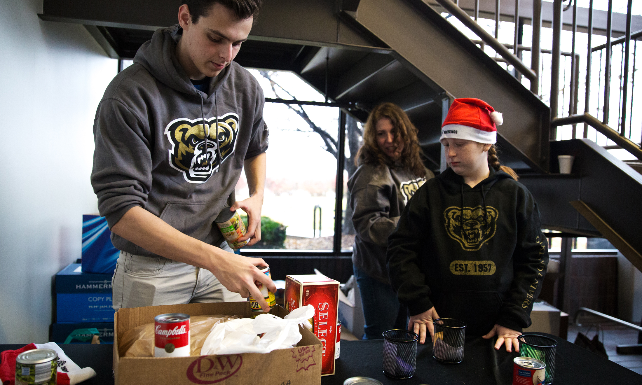 Oakland University student in gray sweatshirt with a golden grizzly head on the front hold cans of food at food drive in Macomb County